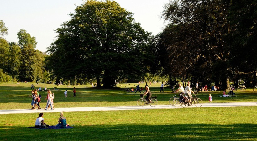 A park with many people riding bikes, having a picnic, and walking.